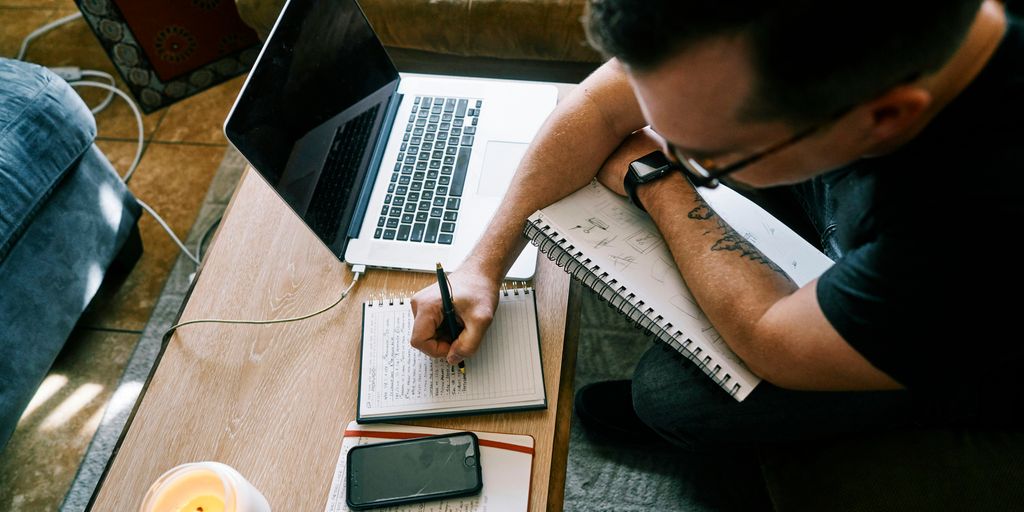 man in black t-shirt writing on white paper