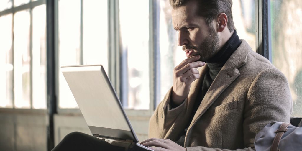 man holding his chin facing laptop computer