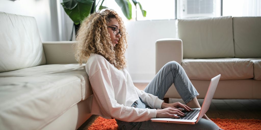 woman sitting on floor and leaning on couch using laptop