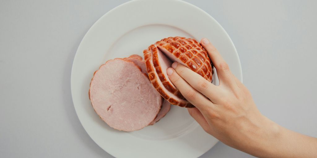 person holding sliced ham in white ceramic plate